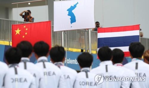 In this file photo from Aug. 26, 2018, members of the unified Korean dragon boat racing team watch the Korean Unification Flag being raised after winning gold medal in the women's 500-meter competition at the 18th Asian Games at Jakabaring Rowing & Canoeing Regatta Course in Palembang, Indonesia. (Yonhap)