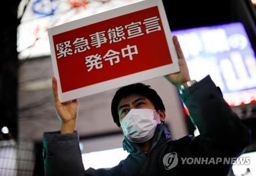 (도쿄 로이터=연합뉴스) 일본 수도권 일부 지역에 신종 코로나바이러스 감염증(코로나19) 긴급사태가 발효한 지난달 8일 오후 도쿄도 직원이 신주쿠(新宿)구의 유흥가에서 '긴급사태선언 발령 중'이라고 적힌 안내판을 들고 있다.