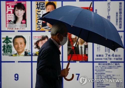 (도쿄 로이터=연합뉴스) 일본 도쿄도(東京都) 의회 선거 투표일인 4일 도쿄에서 마스크를 쓴 유권자가 후보자 포스터가 게시판 앞을 지나고 있다.