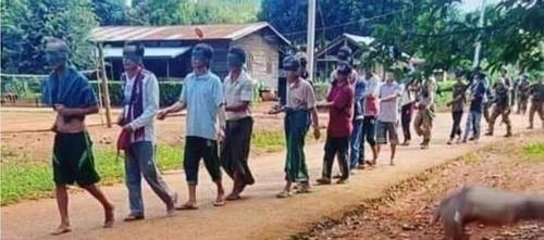 눈을 가린 채 줄에 앞뒤로 묶여 걸어가는 미얀마 시민들. 뒤로 군인들이 보인다