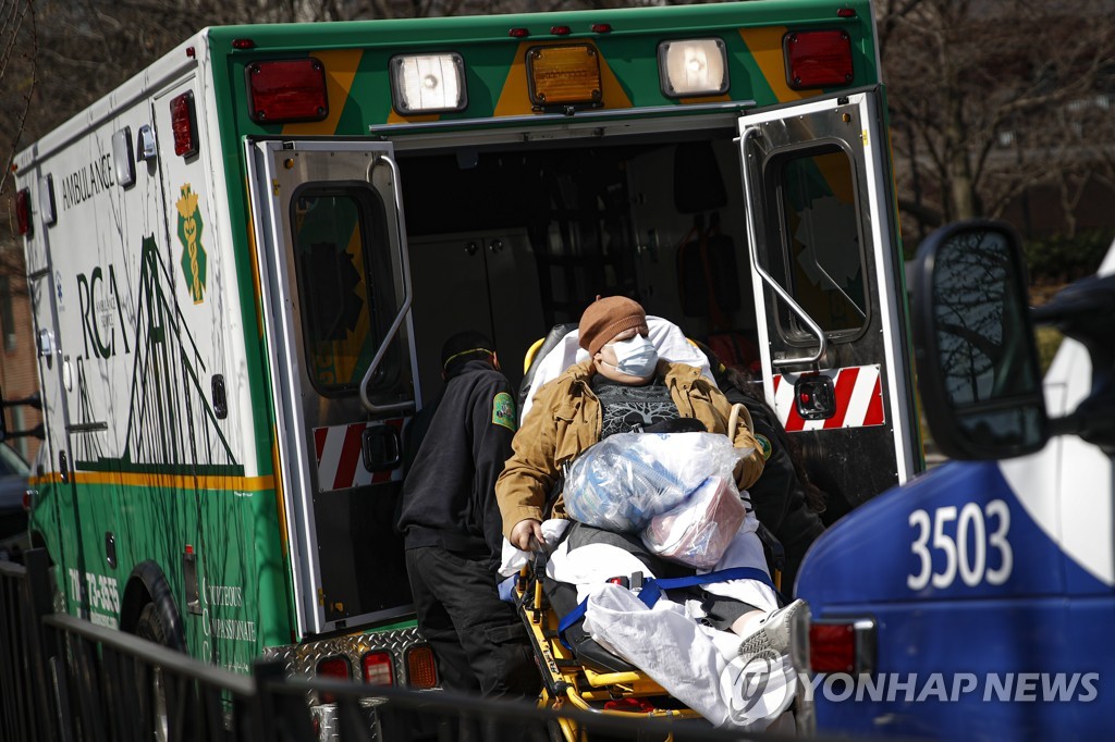 18일(현지시간) 뉴욕 브루클린의 한 병원에서 마스크를 착용한 환자가 응급차량으로 이송되고 있다.