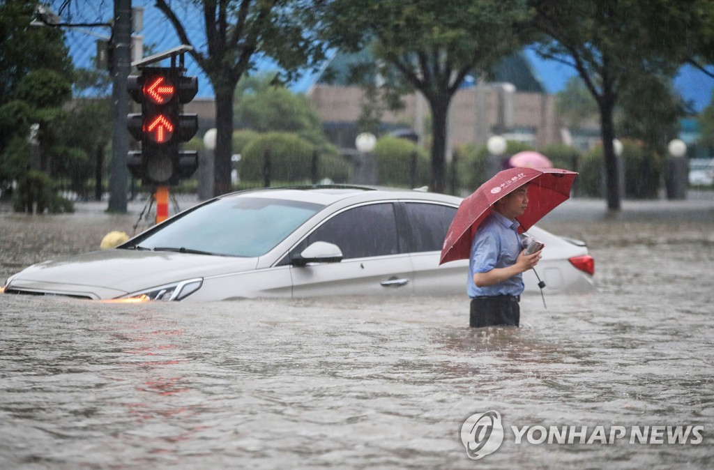 20일 중국 허난성 정저우에서 물에 잠긴 차 앞으로 한 남성이 지나가고 있다. [AFP=연합뉴스]