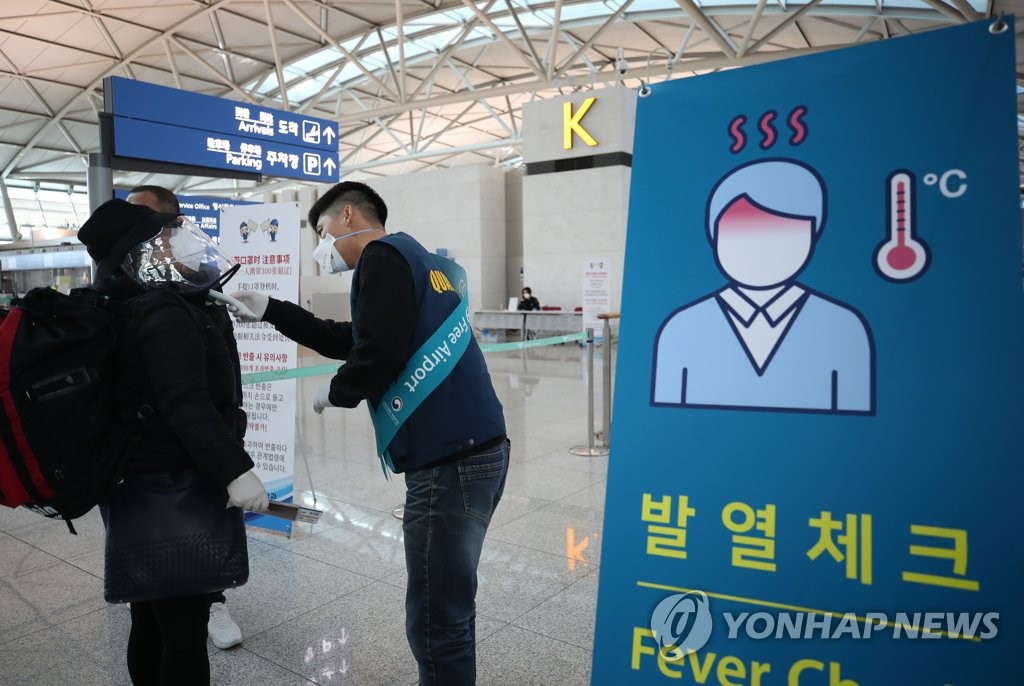 In this file photo taken on March 5, 2020, an official checks the body temperature of a passenger at Incheon International Airport. (Yonhap)