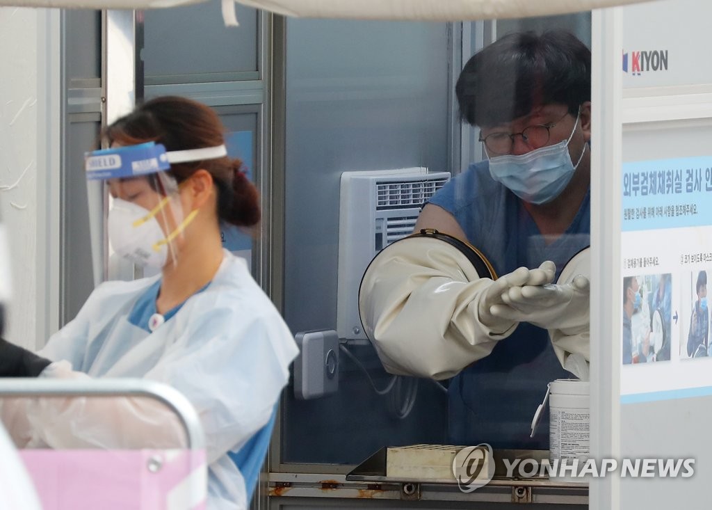 A health worker cleans his gloved hands with sanitizer after collecting a sample for a new coronavirus test at a test center in Seoul. (Yonhap)