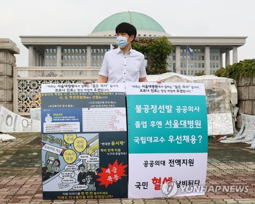 A Seoul National University Hospital trainee doctor holds up signs critical of the government's medical reform plan, in front of the National Assembly in Seoul on Sept. 1, 2020. (Yonhap) 