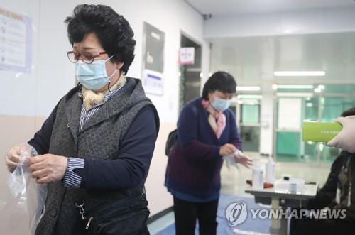 People put on disposable gloves before casting their ballots to protect themselves against the coronavirus at a polling station in the southern port city of Busan on April 7, 2021 (Yonhap) 