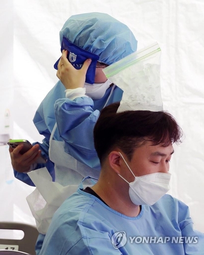 A health worker tries to cool off by putting a plastic bag full of ice cubes on his head at a COVID-19 testing center in Seoul on July 22, 2021. (Yonhap)