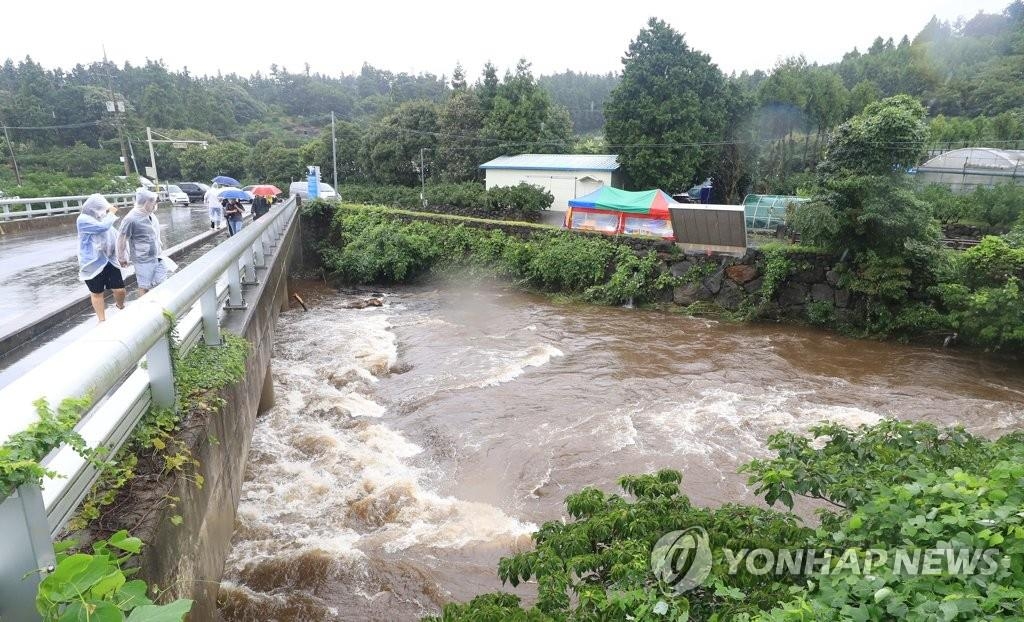 Pedestrians wearing ponchos look at a swollen stream caused by torrential rains on Jeju, South Korea, on Sept. 14, 2021. (Yonhap)