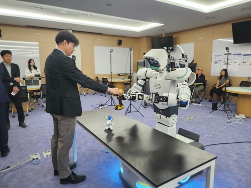 Professor Bae Joon-bum (L) hands a drill to a robot named Avatar at a lab of the Ulsan National Institute of Science and Technology on April 28, 2023. (Yonhap)