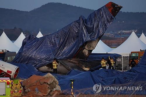 Los bomberos cubren el ala trasera del avión de Jeju Air destrozado con una lona en el lugar del accidente en el Aeropuerto Internacional de Muan en el condado de Muan, provincia de Jeolla del Sur, el 4 de enero de 2025, después de que finalizó la operación de búsqueda. (Yonhap) 