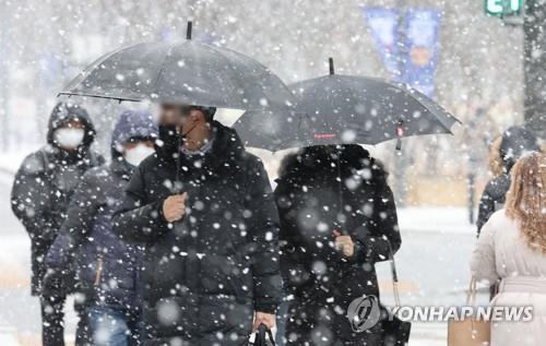 Des citoyens traversent un passage piéton au carrefour de Gwanghwamun, dans le centre de Séoul, sous de gros flocons de neige, le mercredi 19 janvier 2022. 