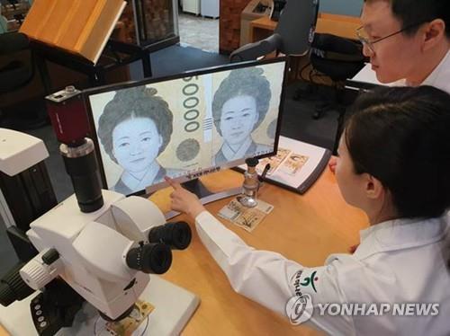 La foto de archivo, sin fechar, muestra a los empleados de un banco, en Seúl, examinando una imagen ampliada de lo que parece ser un billete falso.