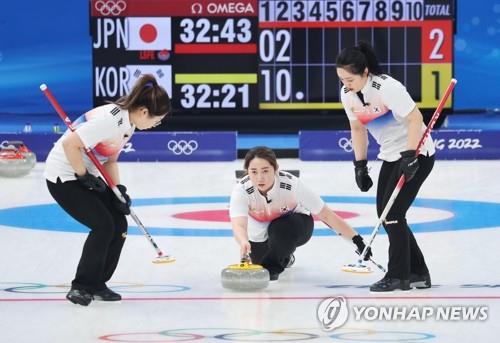 La surcoreana Kim Yeong-mi (centro) lanza la piedra mientras sus compañeras de equipo Kim Seon-yeong (izda.) y Kim Kyeong-ae se preparan para barrer el hielo, durante su partido de fase de liguilla contra Japón, en el torneo de "curling" femenino de los JJ. OO. de Invierno de Pekín, el 14 de febrero de 2022, en el Centro Acuático Nacional, en la capital china.