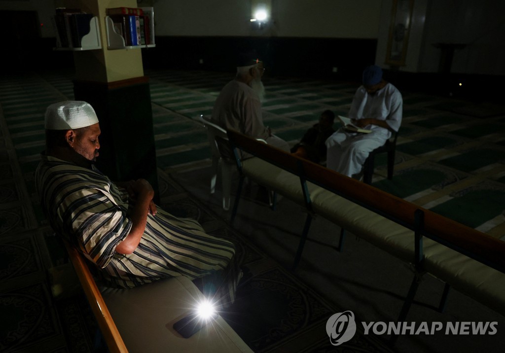 지난 11일 남아공 케이프타운에서 정전 속 모바일폰 불빛을 이용하는 한 무슬림 남성