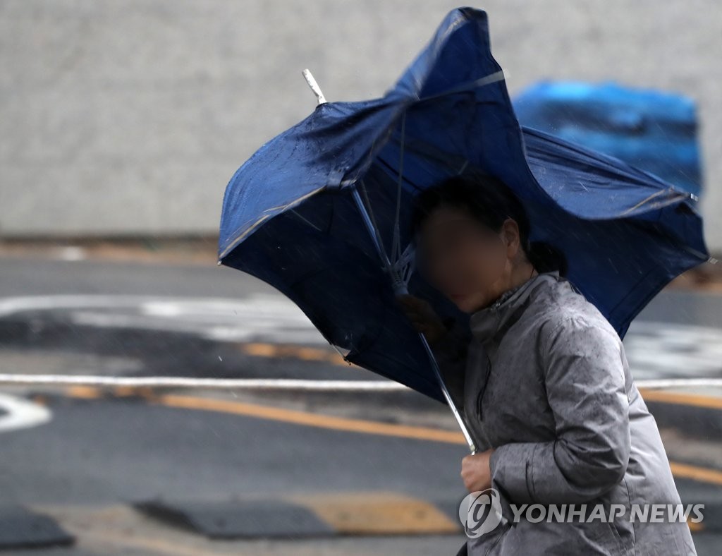 A woman struggles against heavy rain and strong wind on a street in the southeastern port city of Busan on Aug. 6, 2019. (Yonhap)