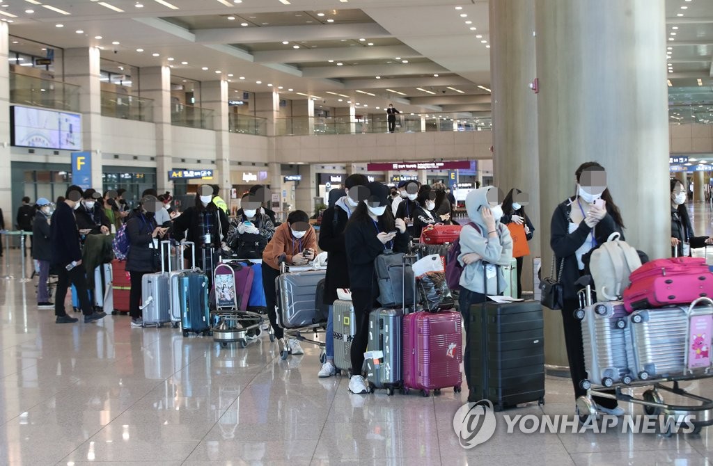 Travelers from London wait in line at Incheon International Airport, west of Seoul, to take a bus heading to virus testing clinics on March 23, 2020. (Yonhap)