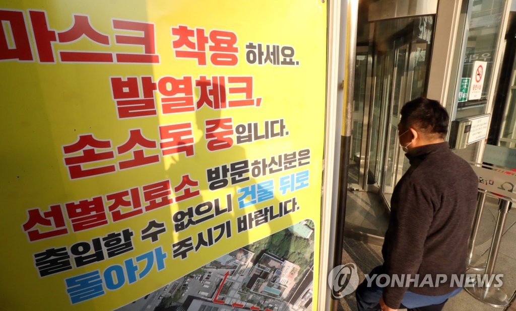 Un ciudadano entra en la Oficina del Distrito de Mapo, en Seúl, el 12 de noviembre de 2020, mientras que en la entrada se muestra un letrero que insta a las personas a utilizar mascarillas protectoras, someterse a exámenes de temperatura corporal y desinfectar sus manos.