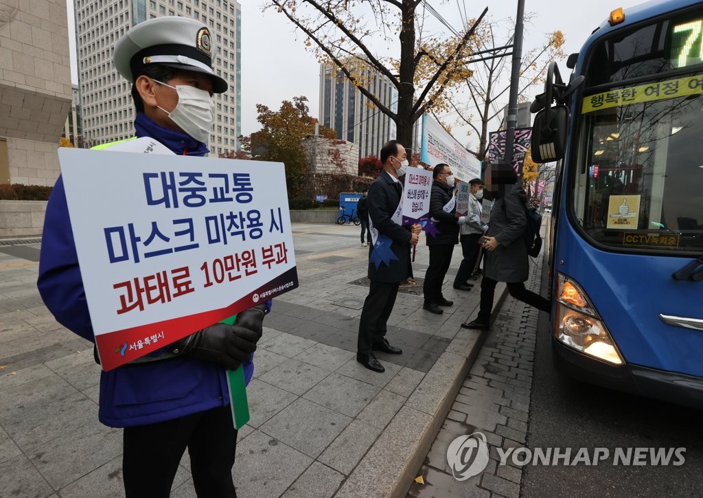 Seoul bus organization officials hold signs calling for people to wear masks when using public transportation in front of a bus station in downtown Seoul on Nov. 13, 2020. (Yonhap)