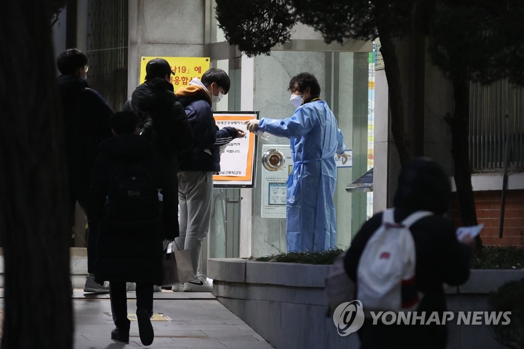 An official gives hand sanitizer to test takers at a high school located in southeastern Seoul ahead of the College Scholastic Ability Test (CSAT) on Dec. 3, 2020. (Yonhap)