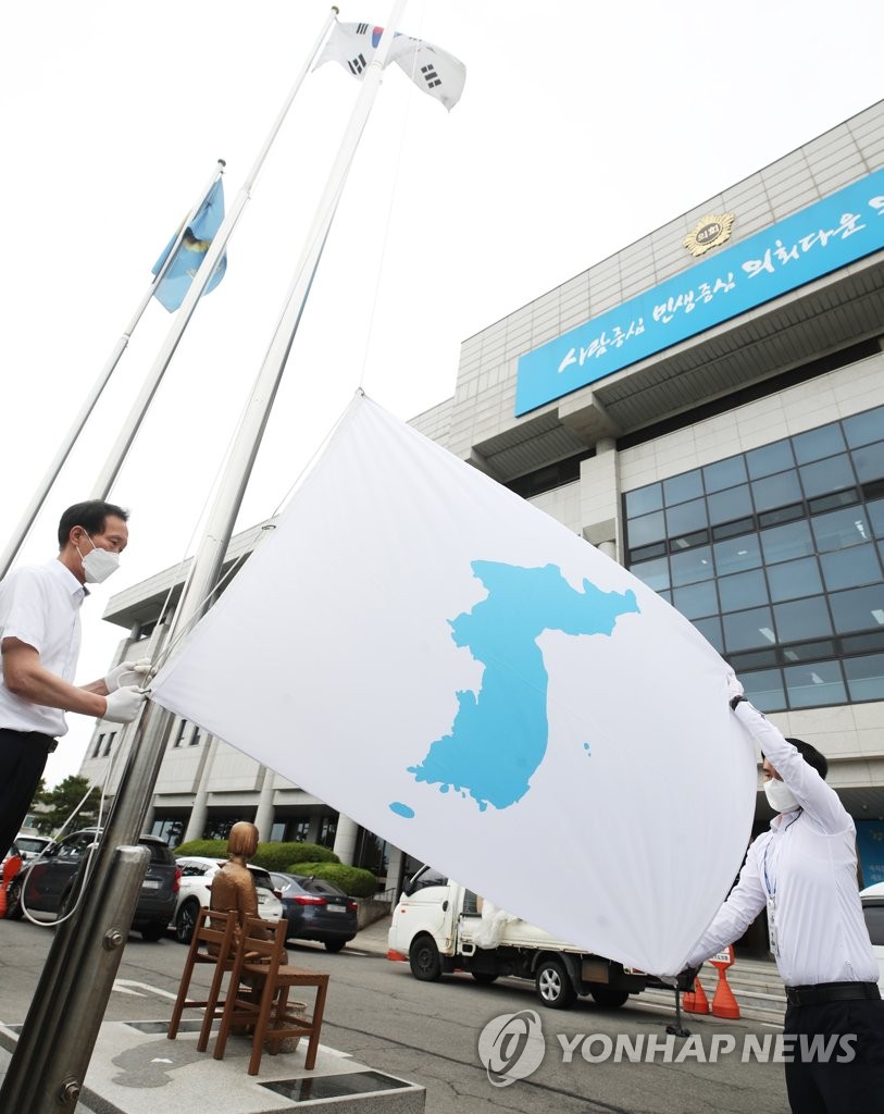 Employees raise a Korean Unification flag, which depicts a blue silhouette of the Korean Peninsula against a white background, at the provincial assembly building in Suwon, Gyeonggi Province, south of Seoul, on June 15, 2021, to mark the 21st anniversary of the first-ever inter-Korean summit held in June 2000 between then South Korean President Kim Dae-jung and North Korean leader Kim Jong-il. (Yonhap)