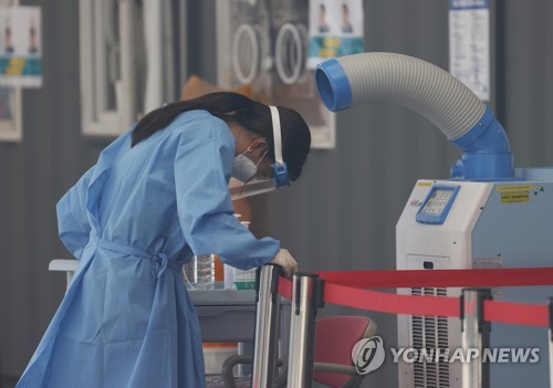 A medical worker at a COVID-19 testing station in Seoul stands in front of an air cooler amid scorching heat on July 2, 2021, when the country reported 826 new infections, including 61 from abroad, the highest in nearly six months. (Yonhap)