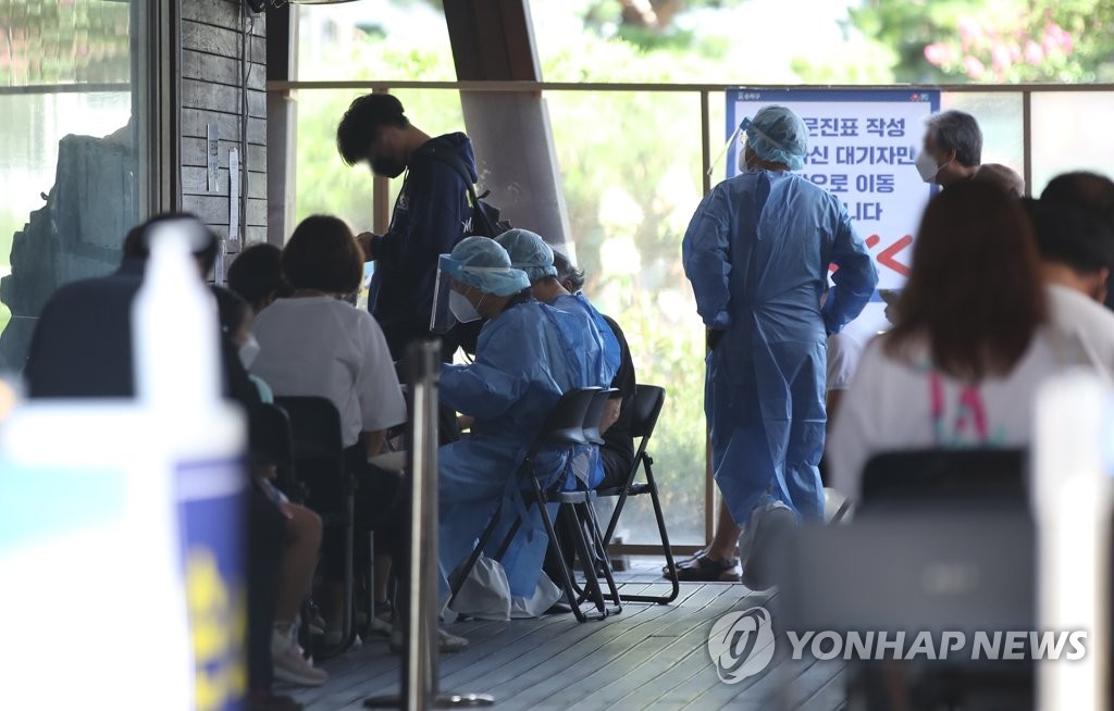 Health workers in protective gear guide people at a makeshift virus testing clinic in Seoul on Aug. 5, 2021. (Yonhap)