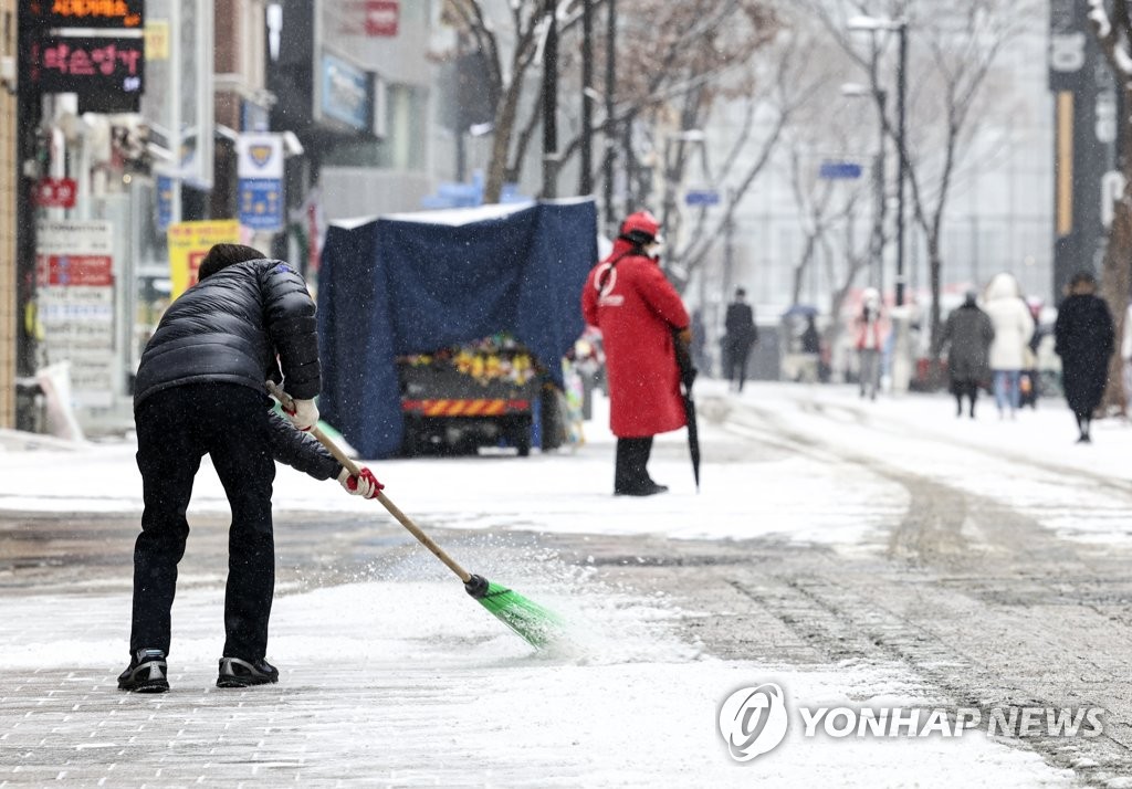 A person sweeps snow off a street in central Seoul on Jan. 19, 2022. (Yonhap)