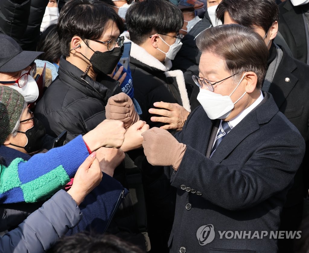 Lee Jae-myung, the presidential candidate of the ruling Democratic Party, bumps fists with supporters at a train station in Busan on Feb. 15, 2022. (Yonhap)