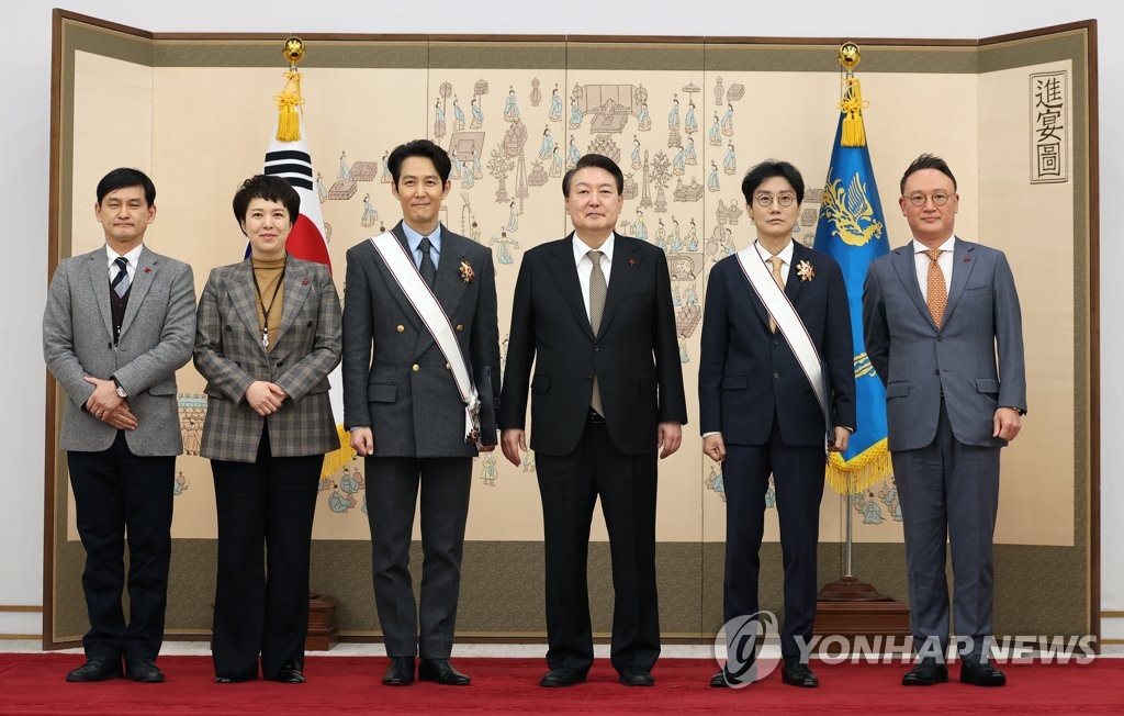President Yoon Suk Yeol (C) poses for a photo with actor Lee Jung-jae (3rd from L) and filmmaker Hwang Dong-hyuk (2nd from R) after conferring the Geumgwan Order of Cultural Merit on them at the presidential office in Seoul on Dec. 27, 2022. (Yonhap)