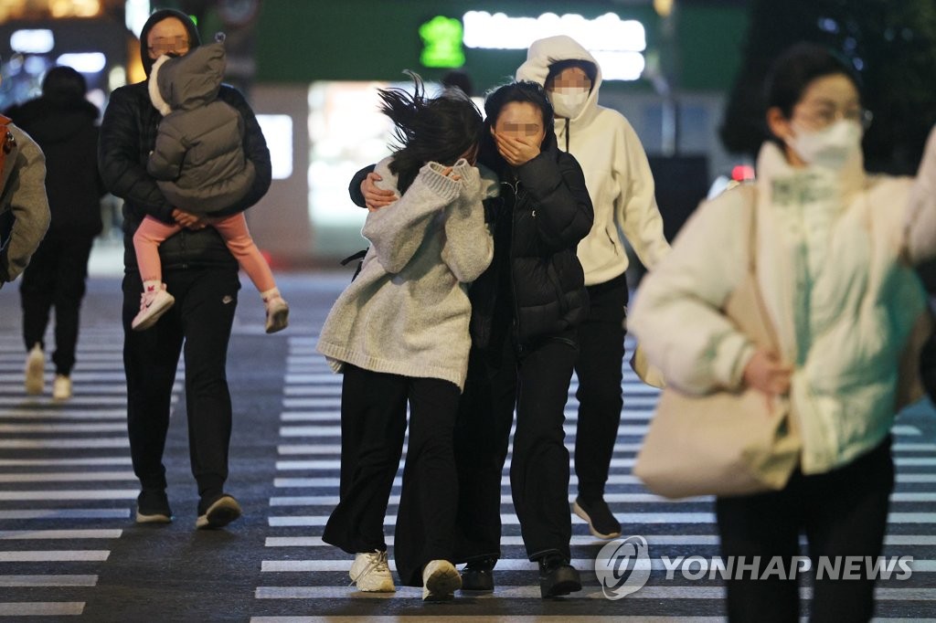 Des gens traversent le dimanche 12 mars 2023 une rue près de la place de Gwanghwamun, dans le centre de Séoul, en affrontant des vents forts.